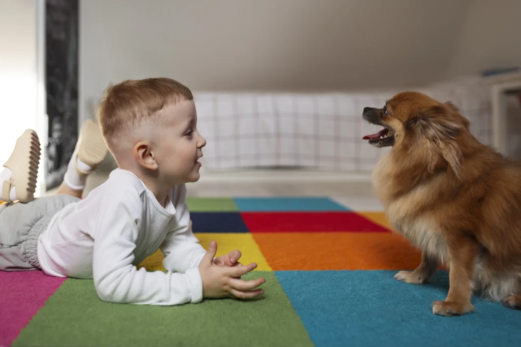  Criança deitada ao lado do cachorro, ambos olhando para o outro com expressão alegre.